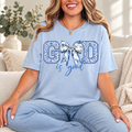 Light blue God Is Good unisex T-shirt with a blue-and-white floral bow graphic, modeled with light-wash jeans.
